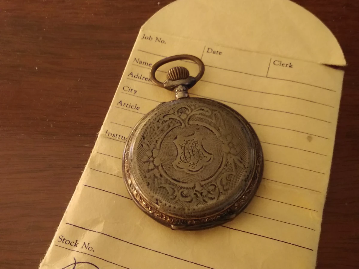 An antique pocket watch resting on a Brown's Jewelers repair envelope